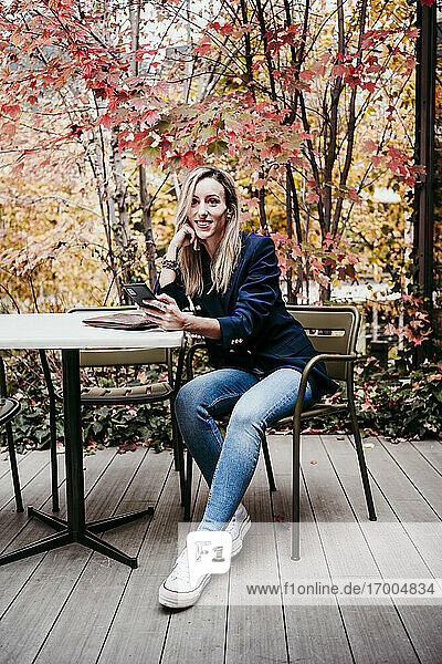 Schöne Frau schaut weg  während sie im Herbst auf der Terrasse sitzt