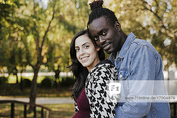 Smiling multi ethnic couple embracing while standing in park