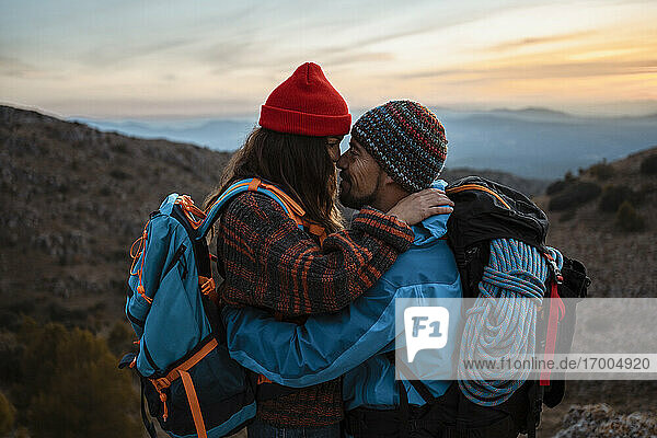Zärtliches Paar steht von Angesicht zu Angesicht auf einem Berg bei Sonnenuntergang