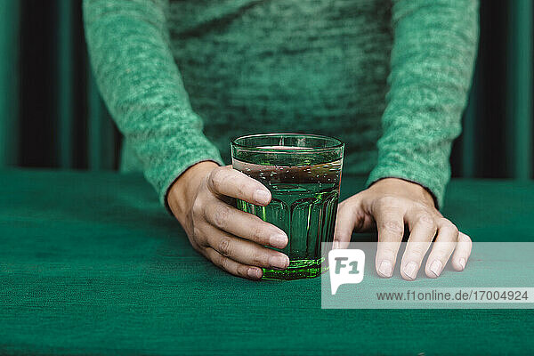 Mittelteil einer Frau  die ein Glas mit einem Cocktail auf einem Tisch hält