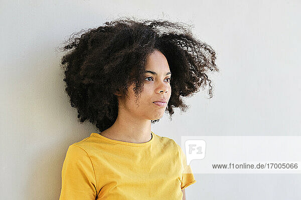 Curly hair student looking away while leaning on white wall