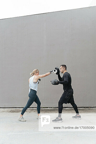 Sportsman teaching boxing to woman while standing against wall