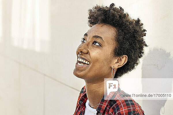 Smiling young Afro female hipster looking up against white wall