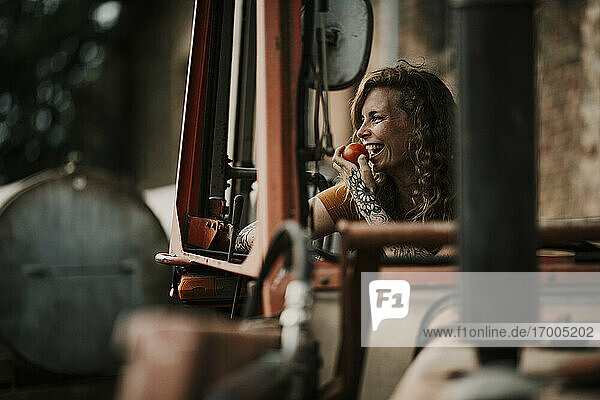 Lächelnde Frau isst Tomate  während sie in einem Traktor sitzt