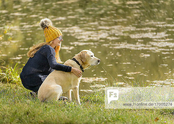 Young woman sitting with Labrador Retriever at lakeshore during autumn