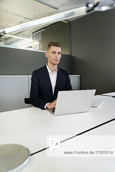 Junger Geschäftsmann mit Laptop schaut weg  während er im Büro sitzt