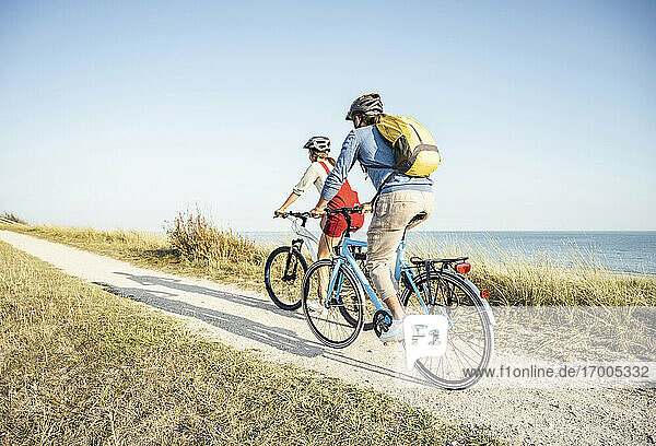 Mann mit Rucksack  der mit einer Frau auf dem Fußweg Fahrrad fährt  an einem sonnigen Tag