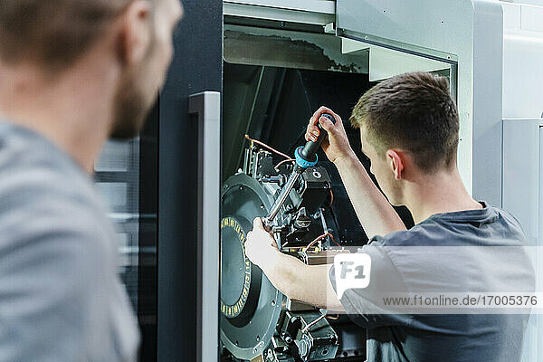 Male trainee fastening bolts of machine while standing at industry