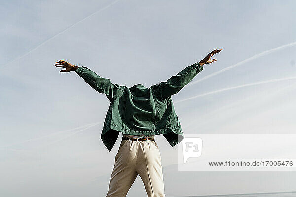 Junger Mann mit ausgestreckten Armen tanzt gegen den Himmel