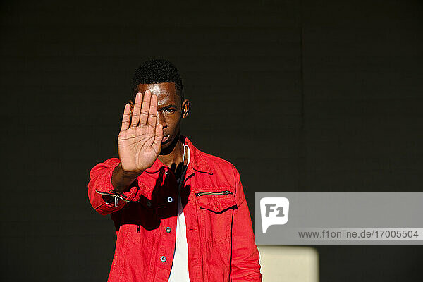 Junger Mann in roter Jacke  der im Sonnenlicht eine Stop-Geste macht