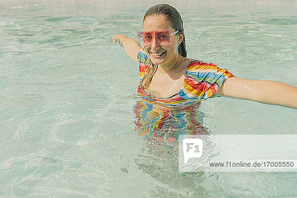 Porträt einer gekleideten Frau mit farbiger Sonnenbrille  die sich im Schwimmbad entspannt