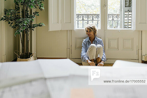Nachdenkliche Unternehmerin schaut weg  während sie im Büro am Fenster sitzt