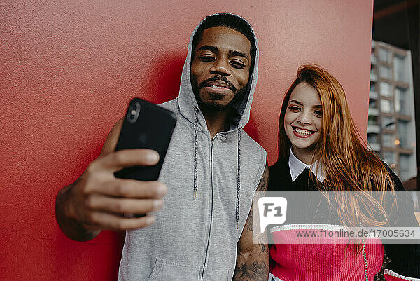 Lächelnde multiethnische Freunde machen ein Selfie vor rotem Hintergrund