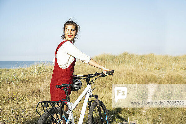 Smiling woman with bicycle walking on footpath