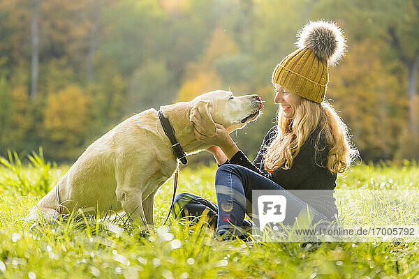 Happy woman playing with canine while sitting in park during autumn season