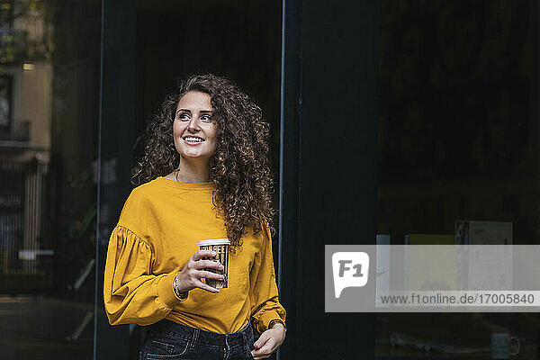 Lächelnde Frau mit lockigem Haar  die eine Kaffeetasse hält und wegschaut