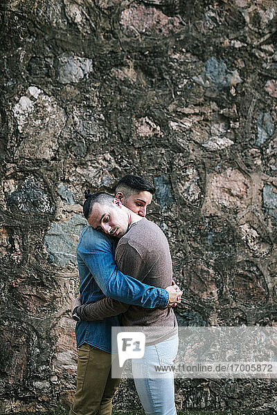 Affectionate gay men embracing each other while standing by stone wall