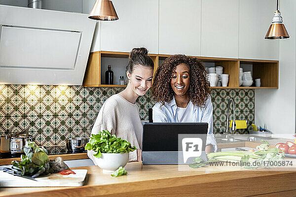 Glückliche weibliche Mitarbeiter  die sich in der Küche am Arbeitsplatz ein Rezept auf einem Tablet ansehen