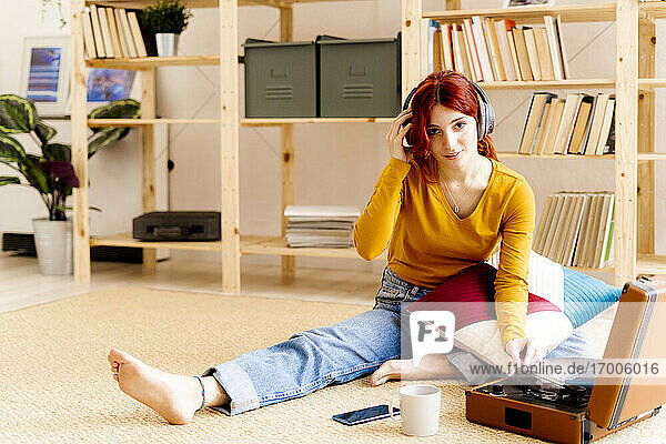 Redhead young wearing headphones using turntable while sitting at home