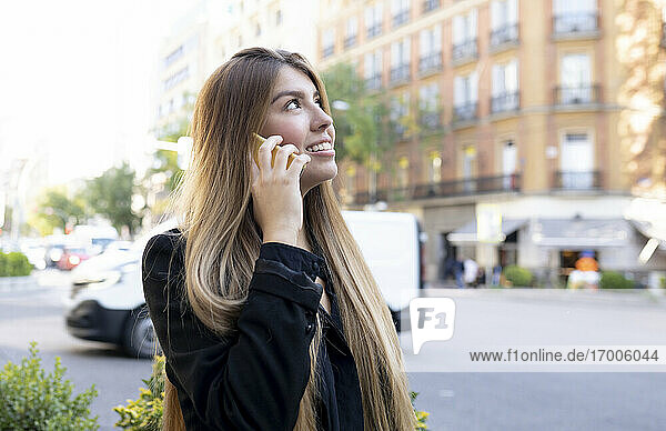 Young woman talking on mobile phone while standing on street in city