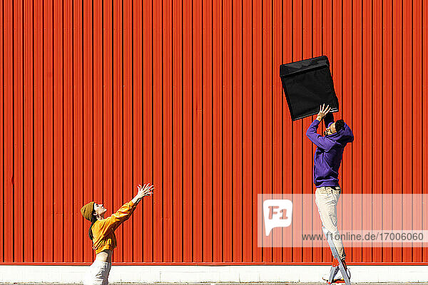 Junger Mann und Frau spielen mit einer Kiste vor einer roten Wand