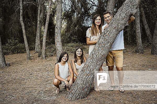 Eltern mit Töchtern stehen hinter einem Baumstamm im Wald