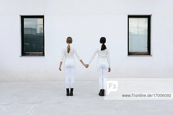 Junge Frauen halten sich an den Händen und stehen vor einem weißen Gebäude