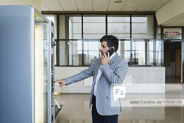 Professor spricht mit dem Handy  während er einen Automaten in der Cafeteria der Universität benutzt