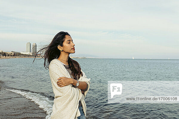 Junge Frau mit verschränkten Armen steht auf dem Wasser gegen den Himmel am Strand