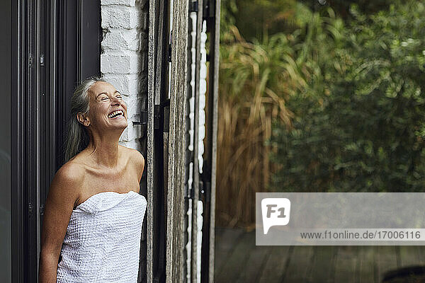 Fröhliche reife Frau mit Handtuch vor einer Haustür stehend