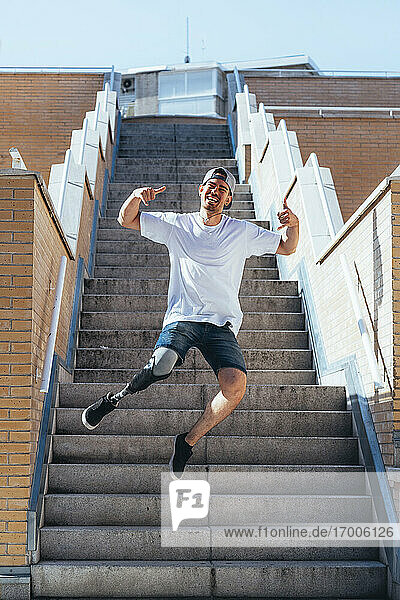 Fröhlicher junger Mann mit Beinprothese springt auf einer Treppe in der Stadt