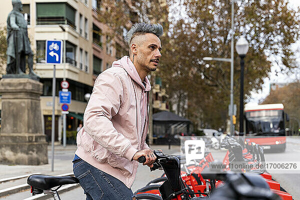 Stilvoller Mann schaut weg  während er ein Fahrrad an einer Parkstation ausleiht