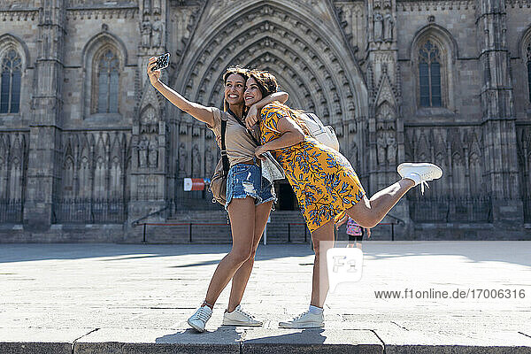 Frau  die ihren Freund umarmt  während sie ein Selfie mit ihrem Mobiltelefon auf dem Platz der Kathedrale von Barcelona in Barcelona  Katalonien  Spanien  macht