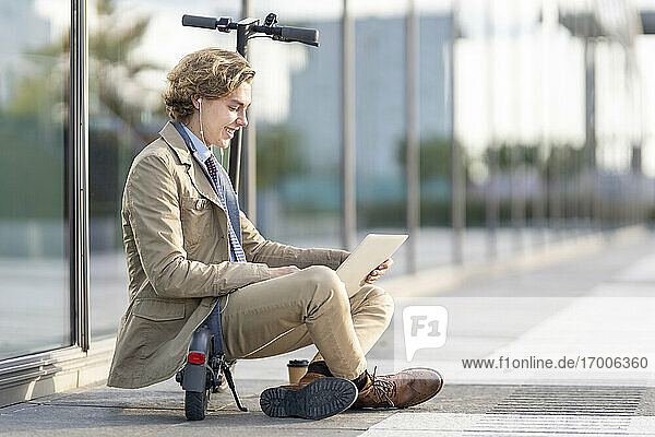 Businessman wearing in-ear headphones using laptop while sitting on electric push scooter