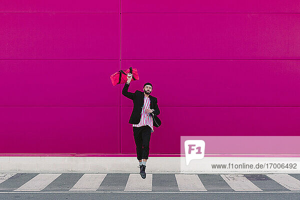 Junger Mann springt mit Reisetasche vor einer rosa Wand