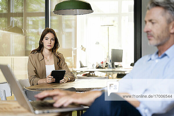 Geschäftsfrau benutzt digitales Tablet  während sie mit einem Kollegen im Büro sitzt