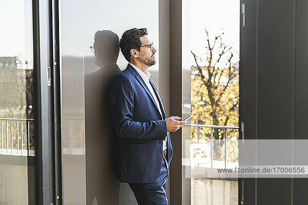 Businessman using mobile phone while standing by balcony at office
