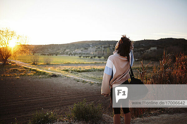 Sportswoman with bag looking at view while leaving after training during sunset