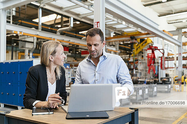 Happy male and female colleagues using laptop at factory