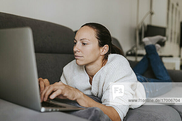 Kaukasische Frau  die einen Laptop benutzt  während sie auf dem Sofa liegt