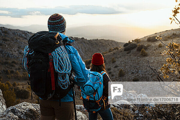 Paar mit Rucksäcken beim Wandern auf einem Berg bei Sonnenuntergang mit Blick auf die Aussicht