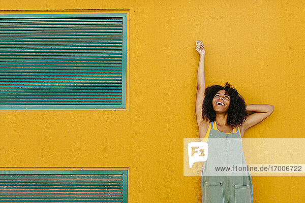 Porträt einer fröhlichen jungen Frau in Latzhose vor einer gelben Wand