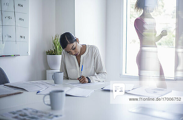 Young businesswoman writing on paper at desk while sitting in office