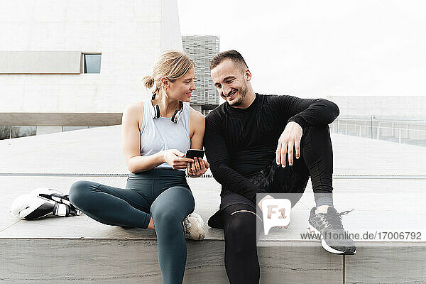 Sportler  der lächelt  während er im Freien sitzend ein Mobiltelefon benutzt