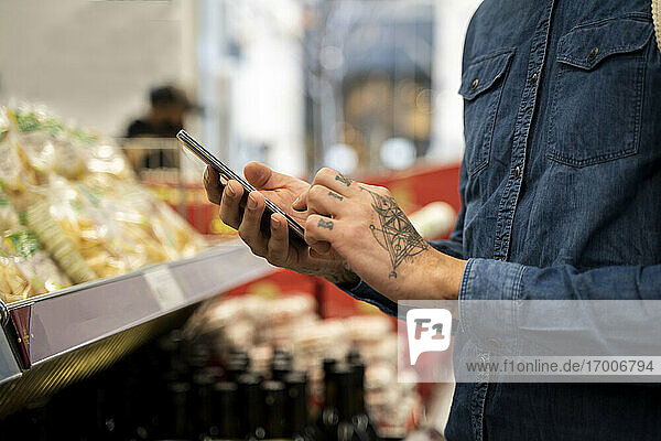 Nahaufnahme eines erwachsenen Mannes  der im Supermarkt ein Smartphone benutzt