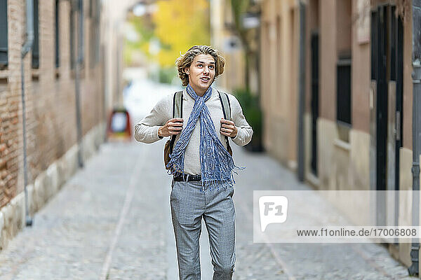 Junger Mann mit Schal  der beim Gehen auf dem Fußweg wegschaut