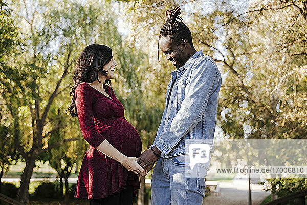 Glücklicher Mann betrachtet den Bauch einer schwangeren Frau im Park