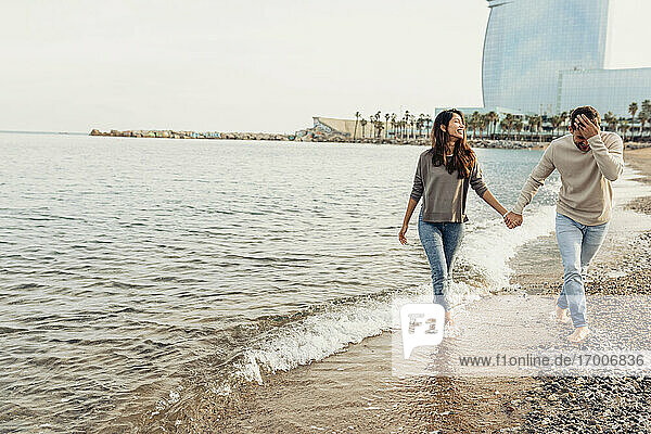 Happy young couple having fun while walking at beach against clear sky