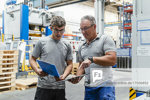 Male coworkers examining product while standing at illuminated factory