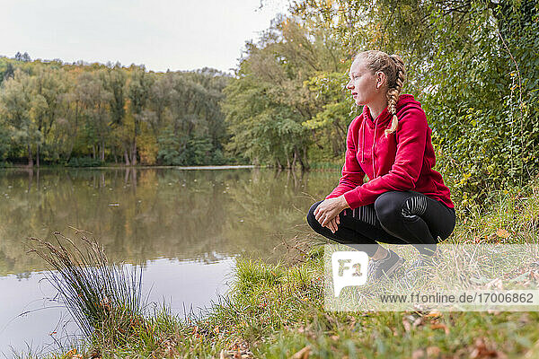 Female athlete crouching while looking at lake in forest